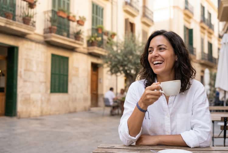 Mujer sonriendo con naturalidad en una terraza soleada de Valencia, reflejo de una sonrisa sana y la confianza de cuidar tu salud bucodental en Valencia